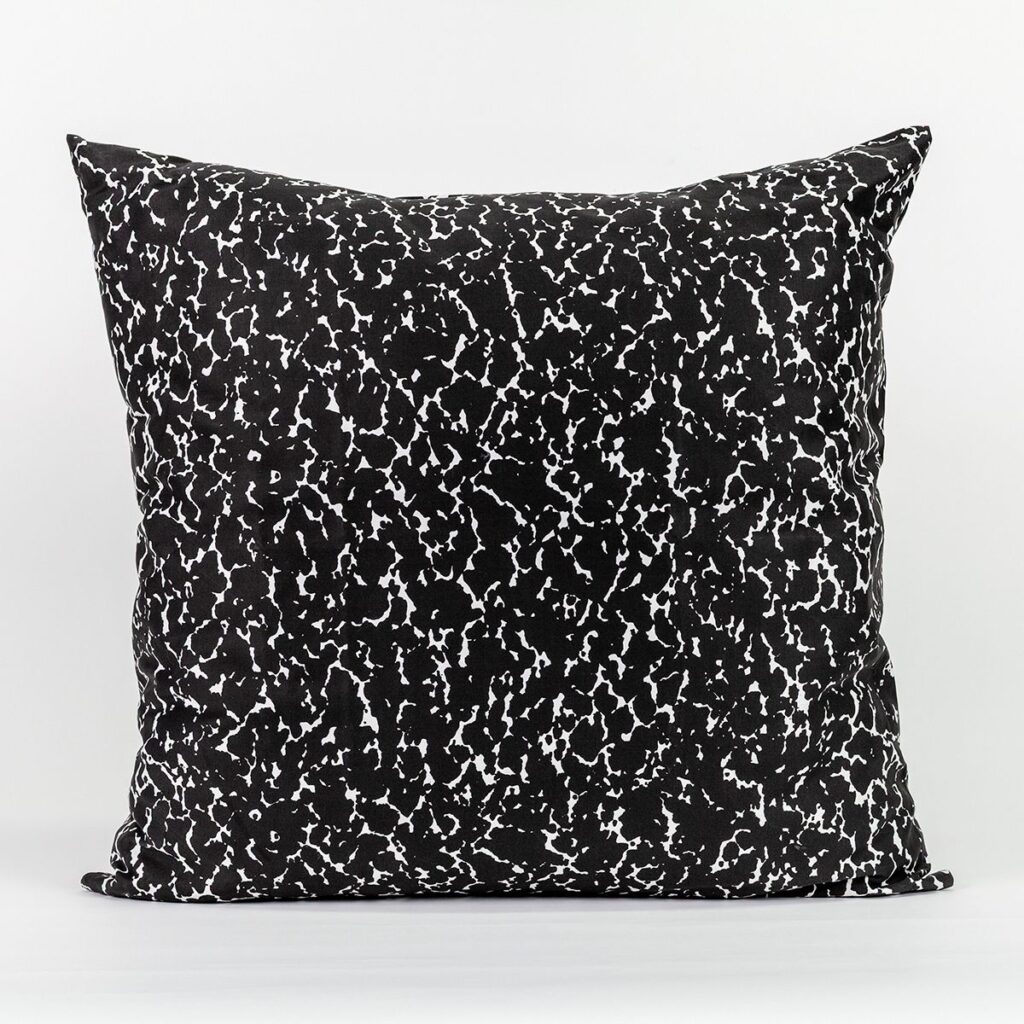 A square pillow with pointy corners featuring a speckled black and white design like the kind found on a student's composition notebook.