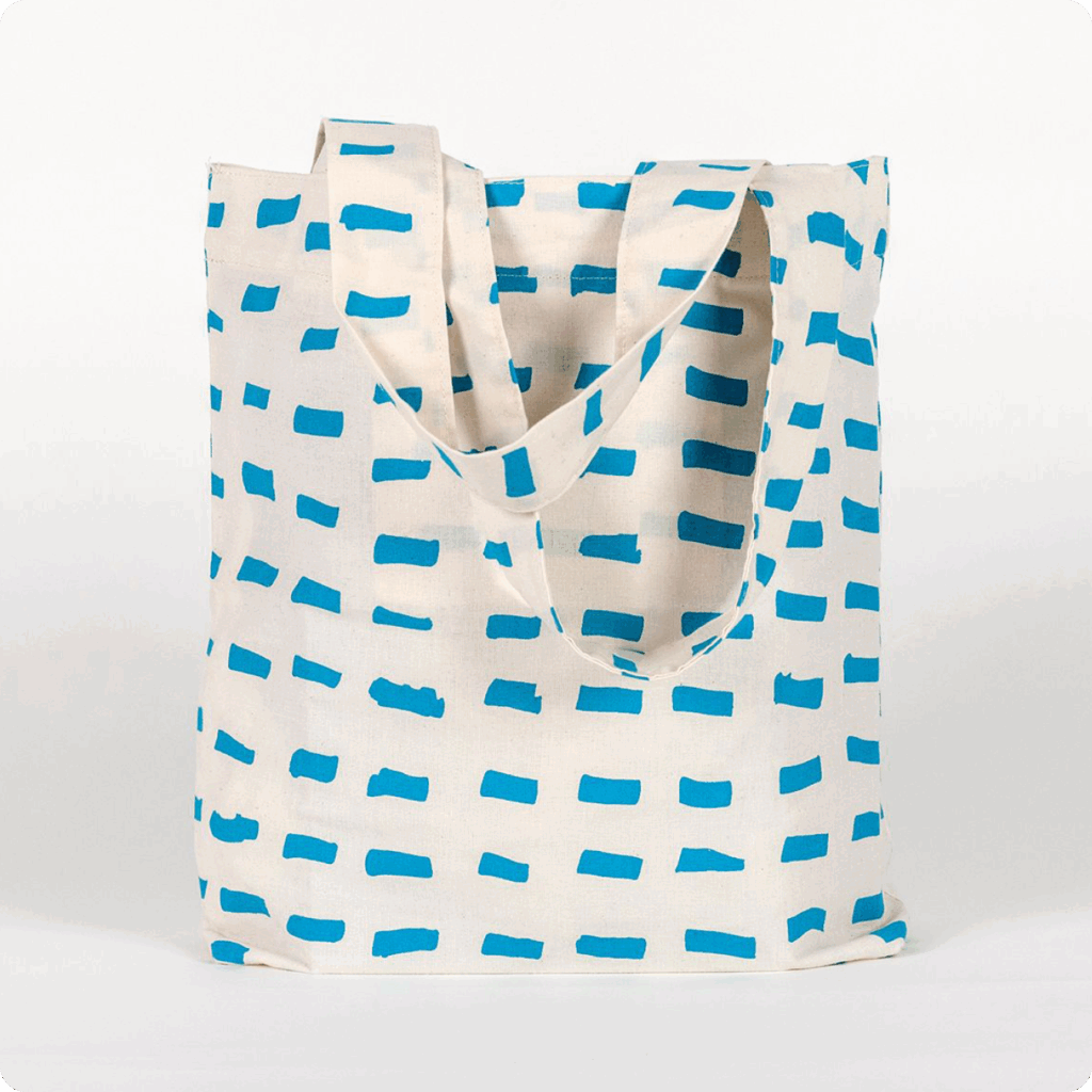 A tall, rectangular tote bag made of white fabric yardage with a printed pattern of short, gestural, brushstroke-like blue dashes.