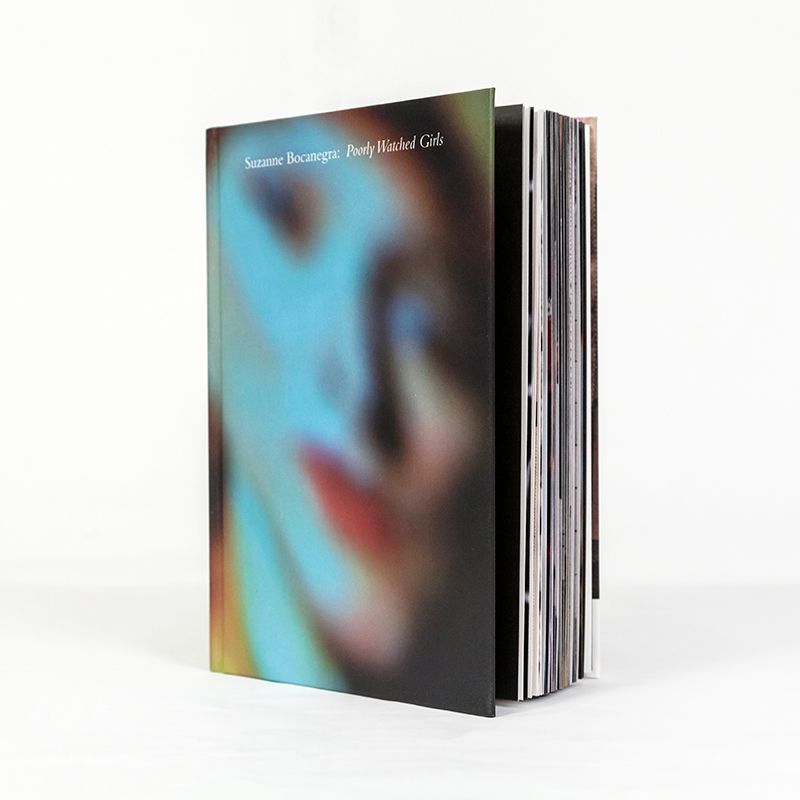 A thick book standing upright, its pages slightly spreading. The cover features an out-of-focus portrait of a person in blue light with red lipstick. The title at the top reads in serif font, 