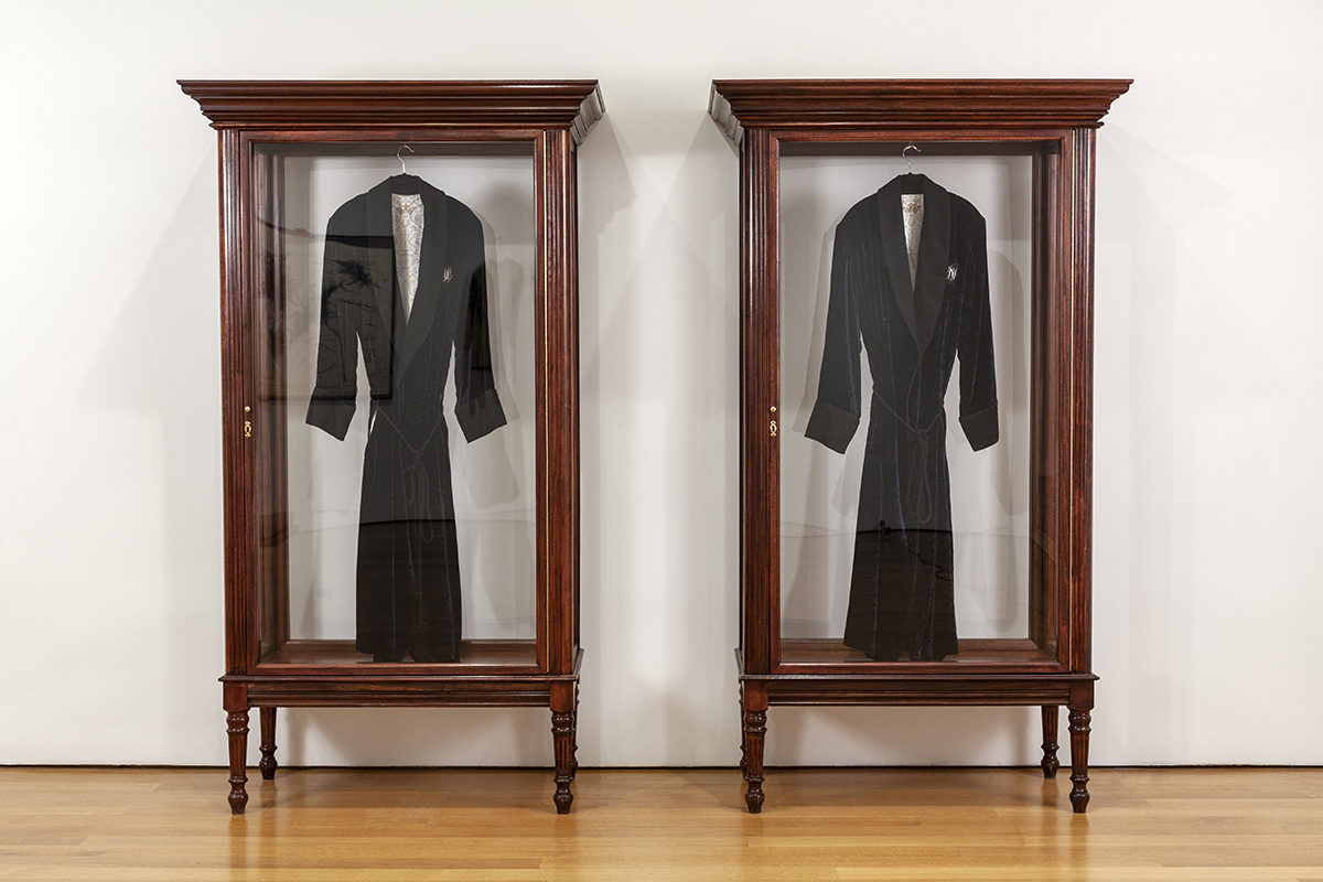 Two large vitrines framed in wood display two identical gentleman's jackets.