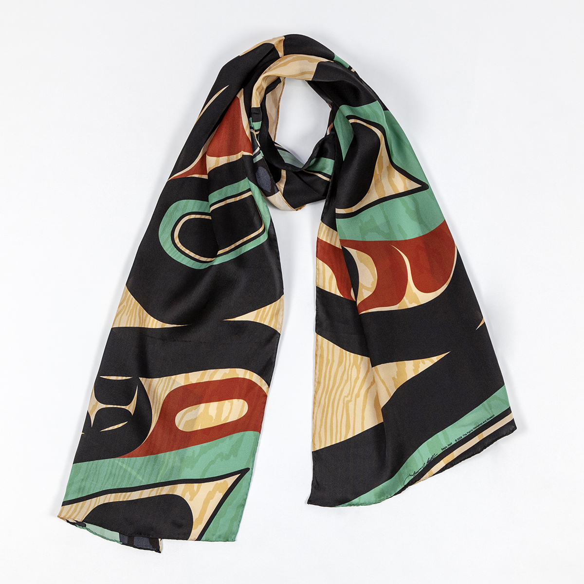 A silk scarf wrapped in a ring shape in the middle to allow room for someone's neck. The scarf is made up of red, teal, and black shapes over a woodgrain colored ground.