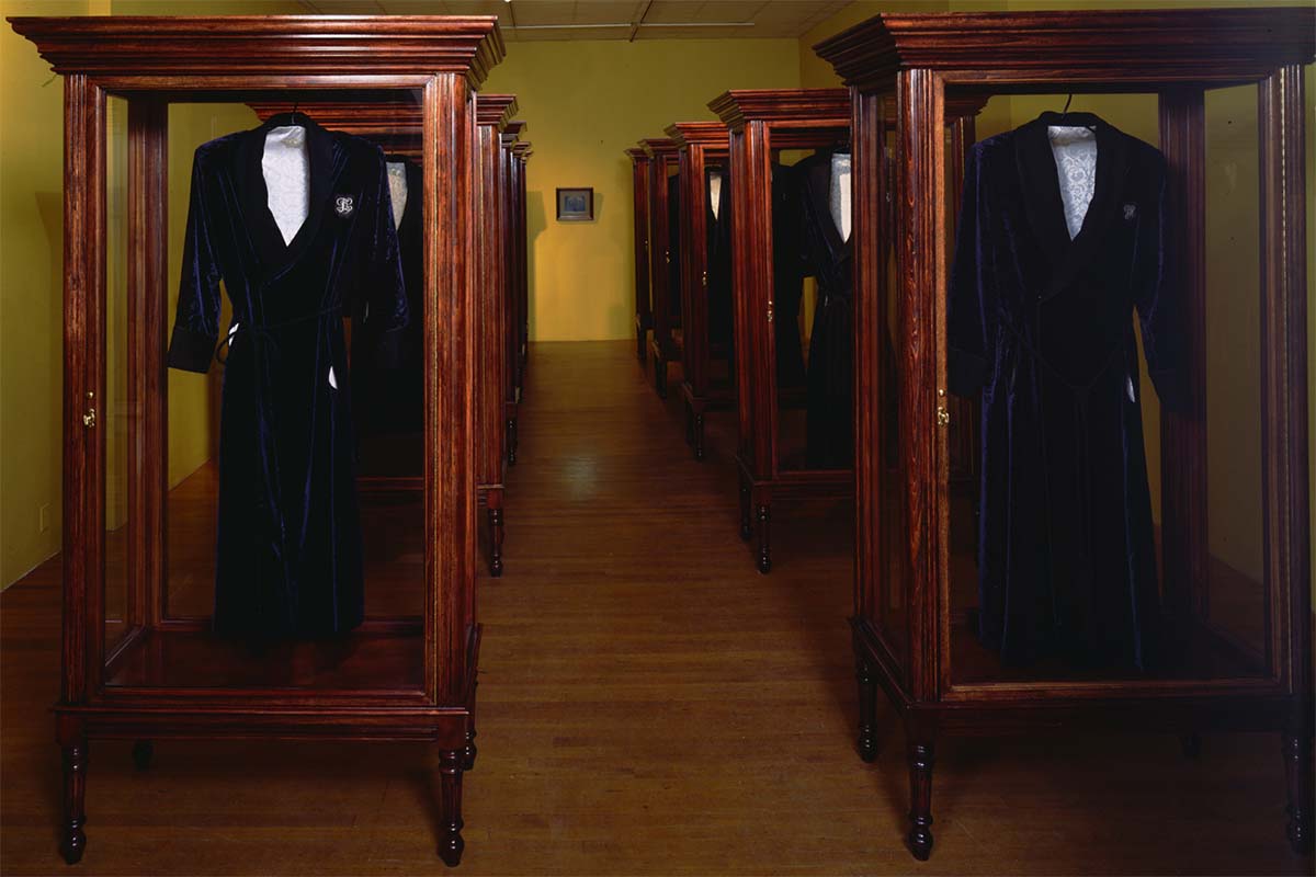 A room of large wooden vitrines display identical gentleman's jackets.