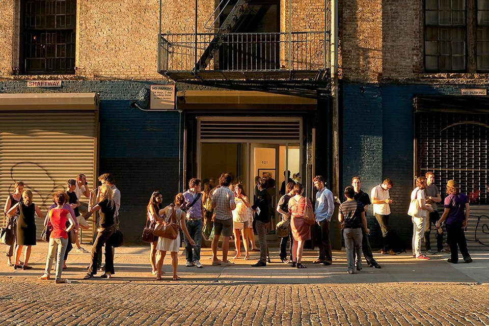 Crowds gather outside a New York gallery during golden hour.