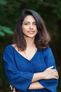 Portrait of Kavyashree Mruthyunjaya Swamy, a young woman of South Asian heritage. She appears to be outdoors and is smiling at the viewer with folded arms. She is wearing a deep blue blouse.
