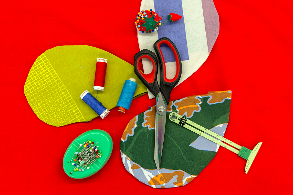 A photograph of a red surface with tear-shaped fabric samples pictured with an array of craft materials including scissors, thread, and sewing pins.