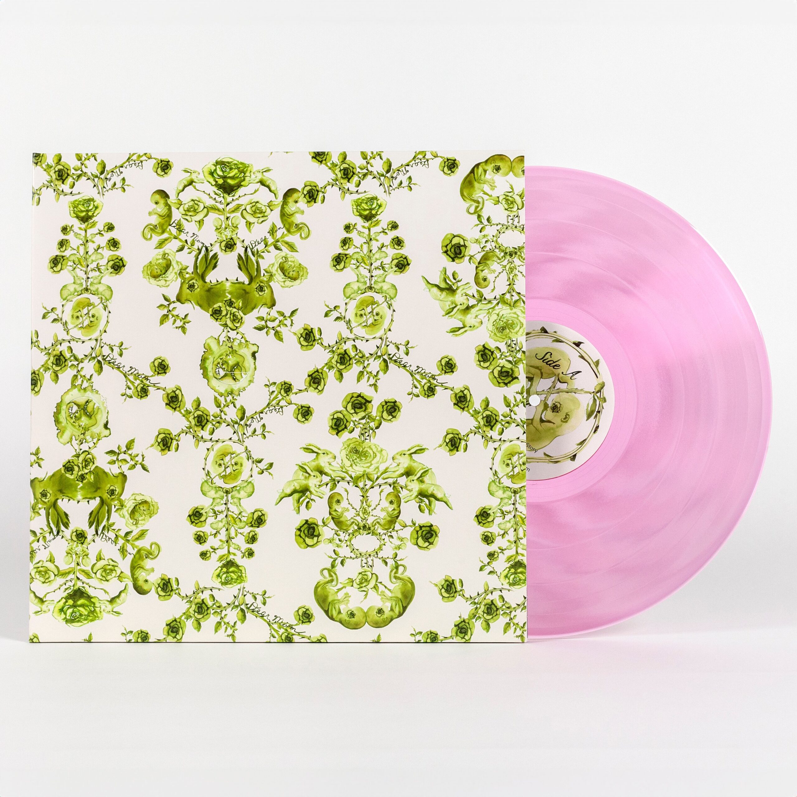 A photo of a vinyl record cover featuring a hand illustrated green toile-like pattern made up mostly of roses but also features twin fetuses and rabbits. This motif is on a solid cream background. Sticking out of the cover is a see-through pink vinyl record that reads 