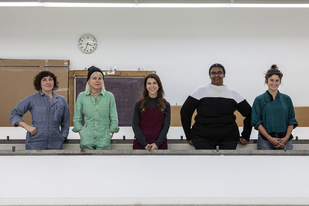 A photograph of FWM's Spring 2024 College Post Graduate Apprentices in the Print Studio. From left to right are artists Lucy Pistilli, Marcella Marsella, Kaitlin Santoro, Lina Elmalik, Jenny Hersh, each facing the camera.