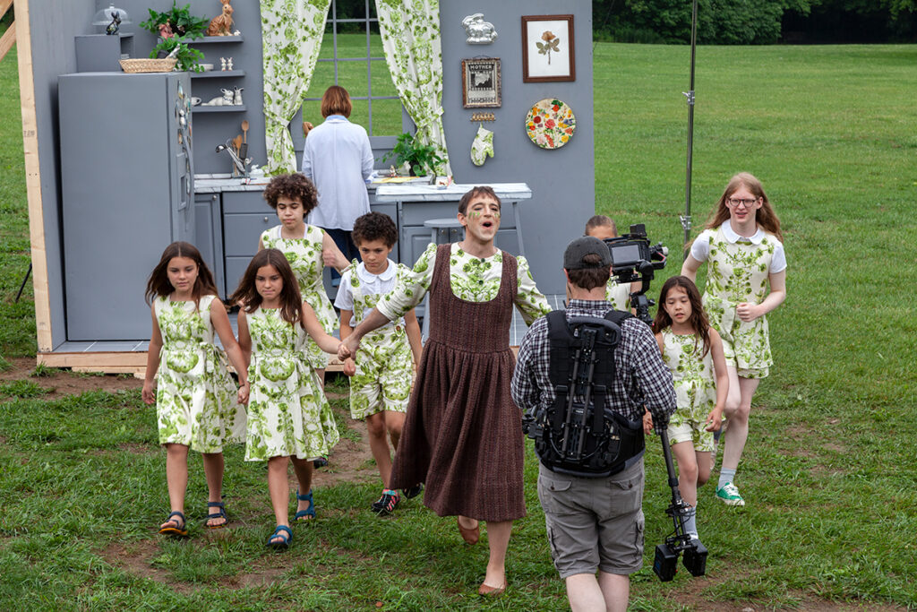 An on-set photograph taken during the filming of “Dear Mom" shows the artist in the center leading a group of child actors hand-in-hand. A videographer with camera equipment is just ahead of them, walking backwards as the group moves forward.