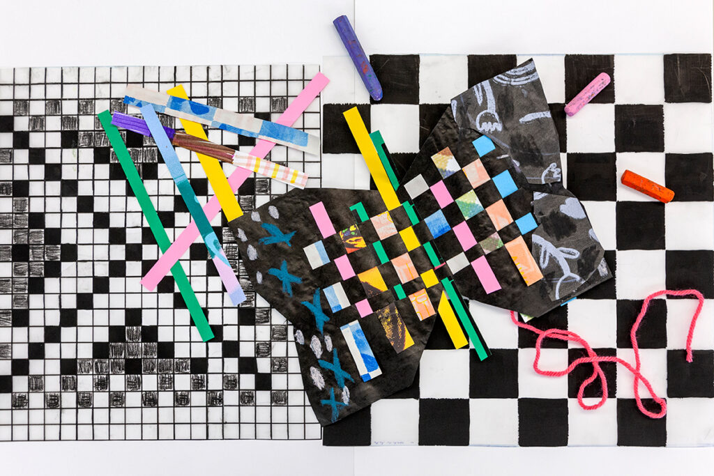 A black butterfly-shaped sheet of paper with a grid of colorful strips of paper woven through it lies atop two other sheets of paper with black and white grids. Extra strips of colorful paper lie scattered over the pattern on the left.