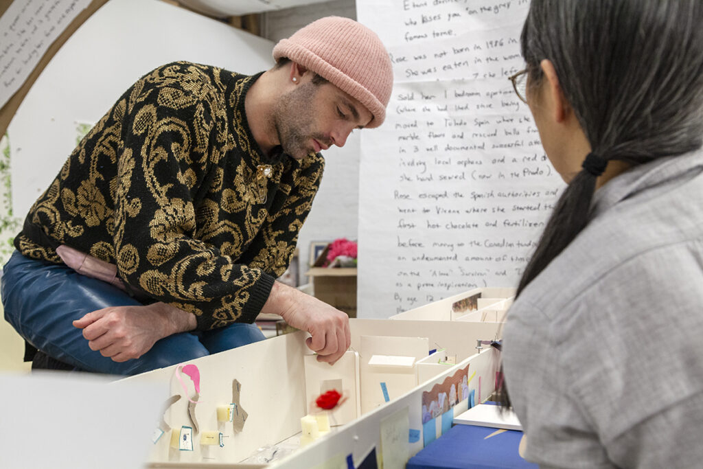 Two artists look over a scale model of a gallery made of foamcore pieces.