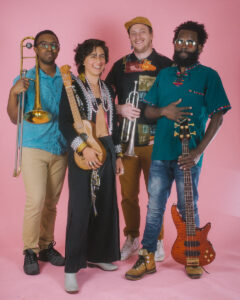 A band of four musicians posing for a portrait with their respective instruments, including horn and string instruments.