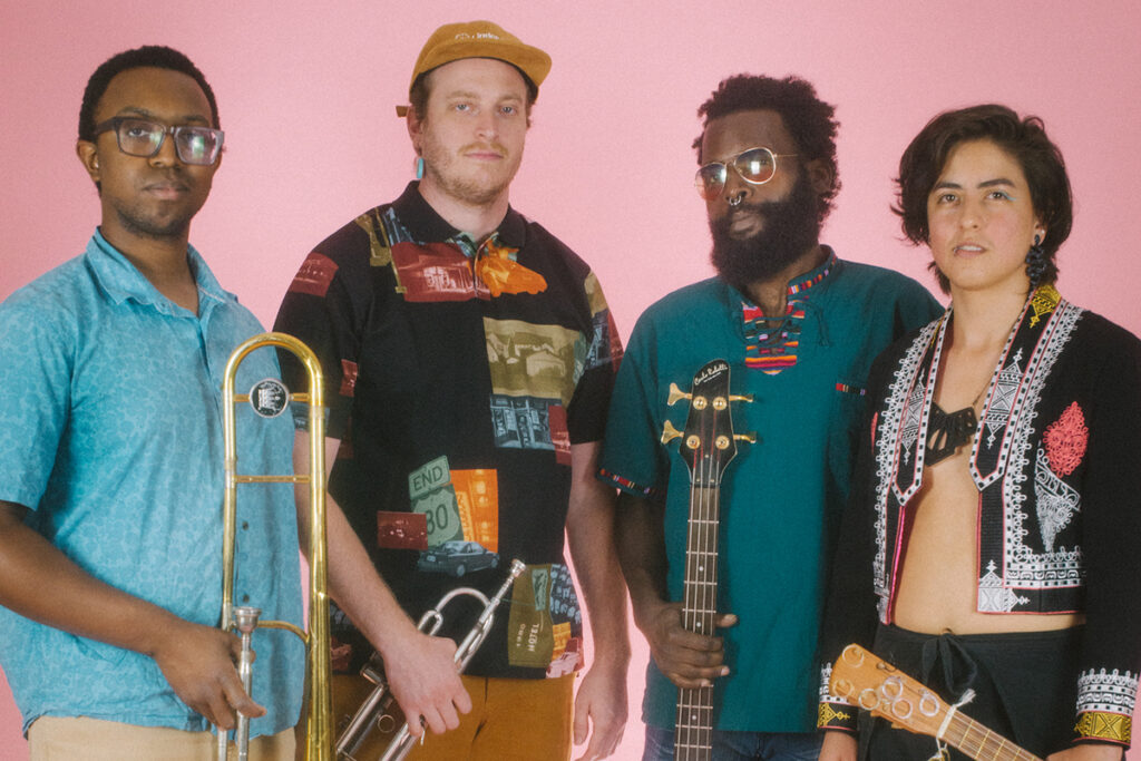 A band of four musicians known as Interminable posing for a portrait with their respective instruments, including horn and string instruments.