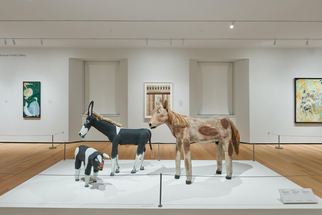 An installation view of the God and Country exhibit featuring three stylized sculptures of a horse, donkey, and pig.