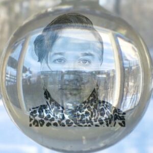 A spherical ornament reflects an environment around it while appearing to hold a portrait of Harmon dot aut, a white person with coiffed hair.