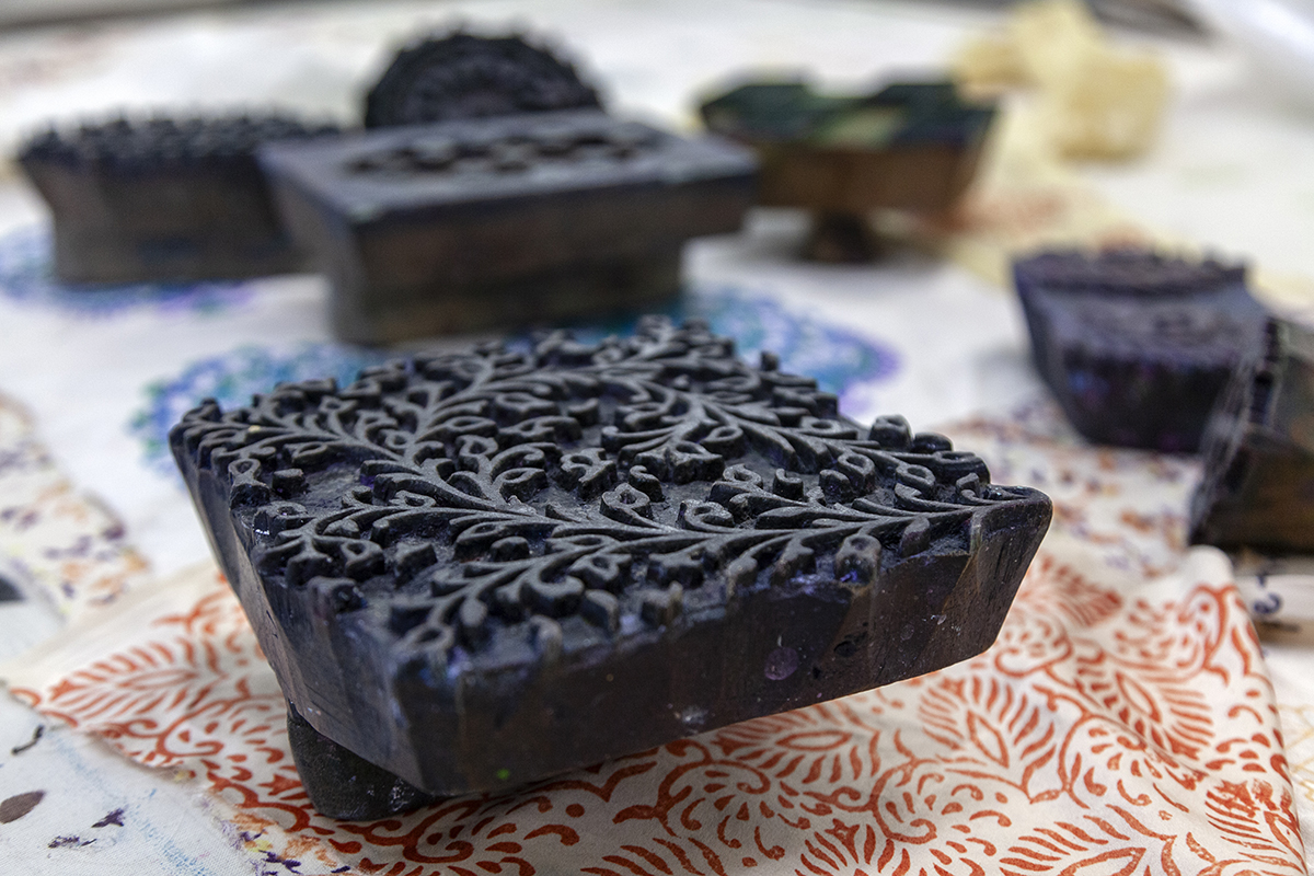 A detailed photograph of an arrangement of wood blocks. Each block has a different carved design. The block in the foreground is square and has an illustrative, lush, floral motif.