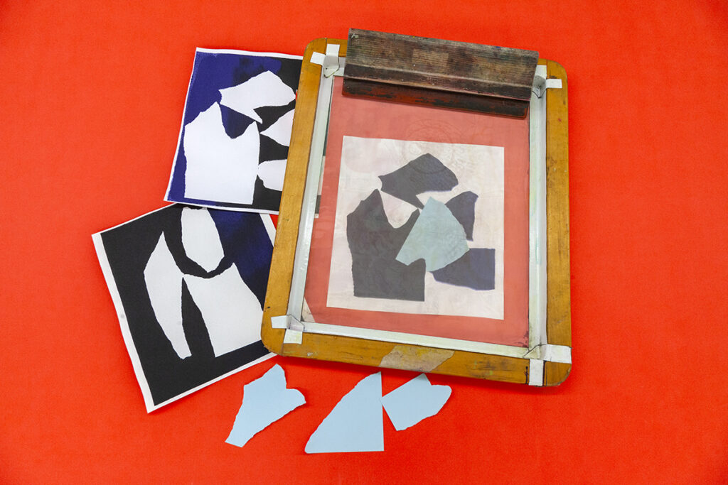 An abstract composition of torn paper shapes appears on two sheets of paper and a silkscreen against a red ground. Three torn light blue paper shapes rest nearby.