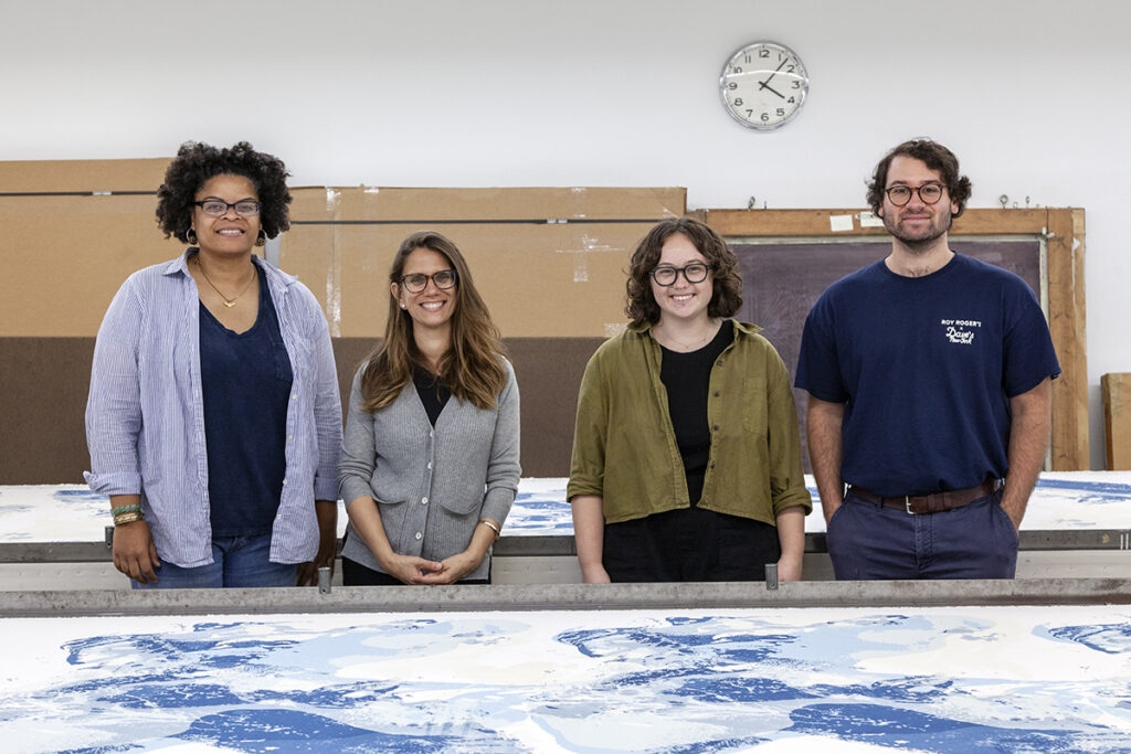 A photograph of FWM's Fall 2024 College Post Graduate Apprentices in the Print Studio. From left to right are artists Athena Scott, Jessica Eldredge, Hannah Zartman, and Henry Rosenberg, each facing the camera.