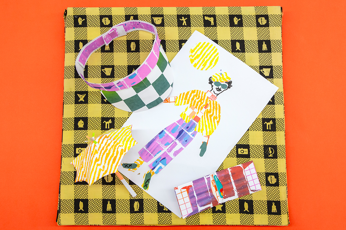 An assortment of printed drawings and objects featuring colorful patterns, such as a drawn figure, a visor, and a small umbrella, lies across a checkerboard pattern.