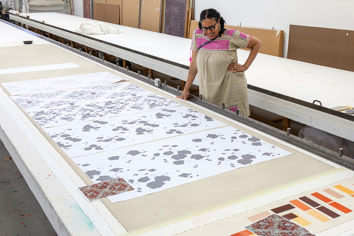 The artist Mildred Beltré Martinez, a Black woman, stands near a sampling of printed patterns and color swatches.