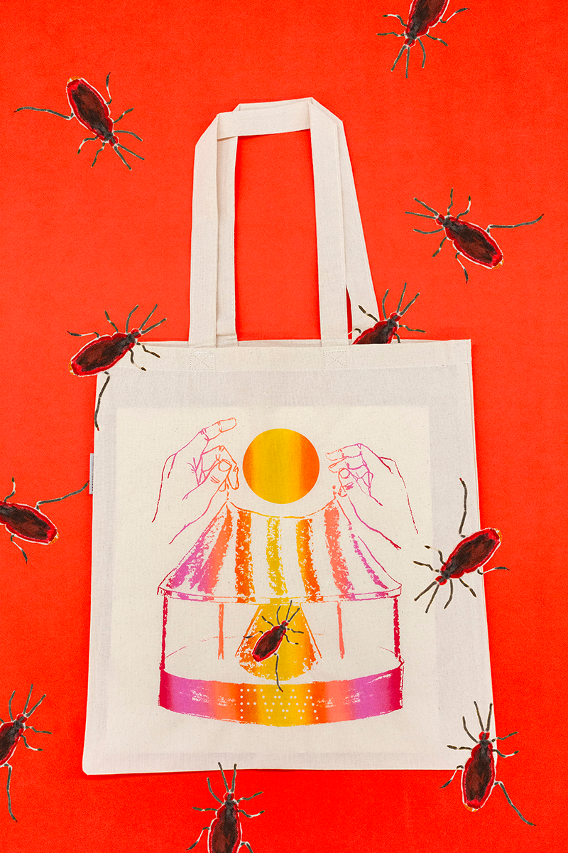 A cream-colored tote lies against a bright orange background. Drawn roaches appear scattered across the image. A drawing of hands playing with a tent-like structure is printed on the tote.