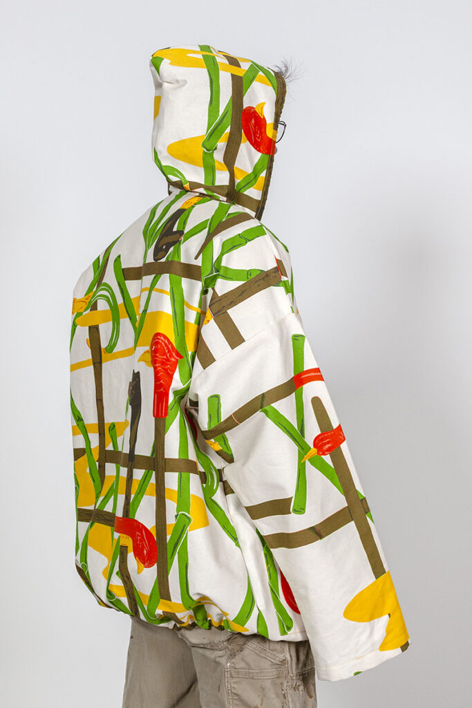 A photo of a model wearing a hooded jacket with a screenprinted pattern of birds and bamboo.
