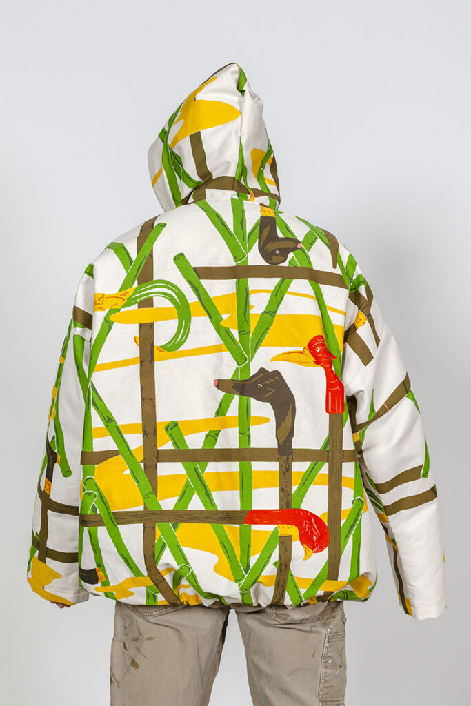A photo of a model wearing a hooded jacket with a screenprinted pattern of birds and bamboo.