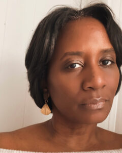 A portrait of Naisha Tyler, a Black Woman with short center-parted hair and gold fan-shaped earrings.