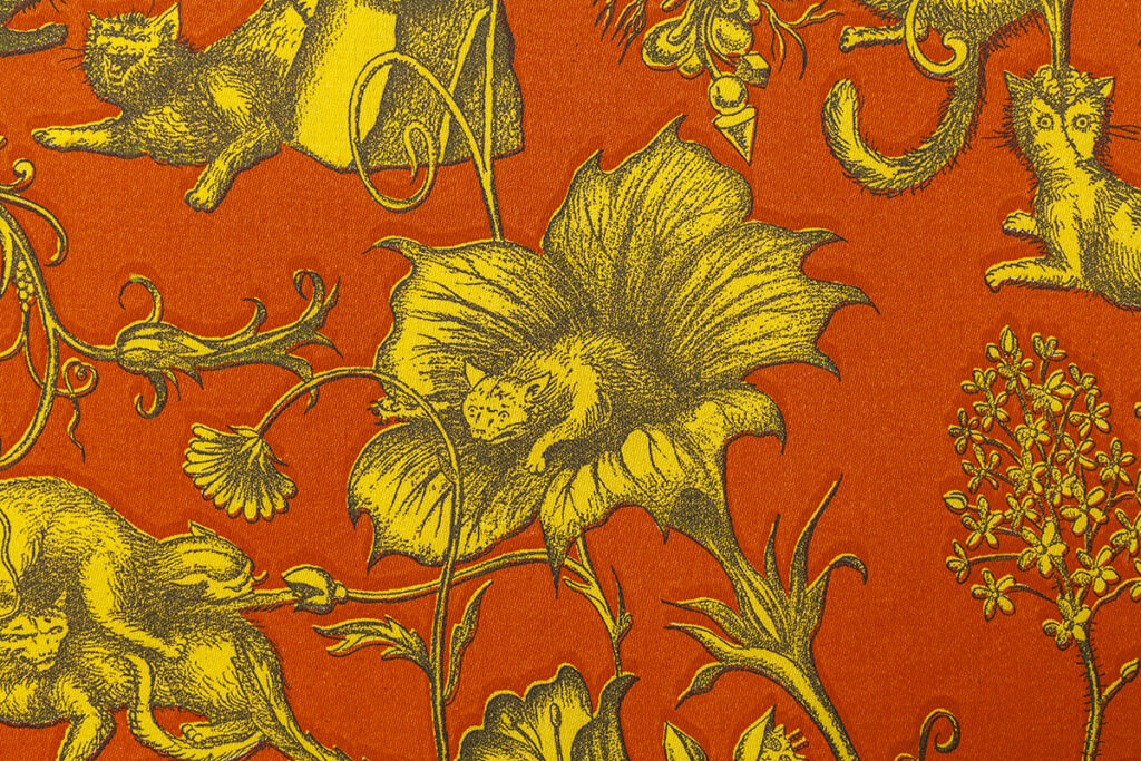 A detail of an illustrated pattern featuring a cat emerging from a large flower. The pattern is composed of three basic colors with a red/orange ground, yellow characters, and dark gray details.