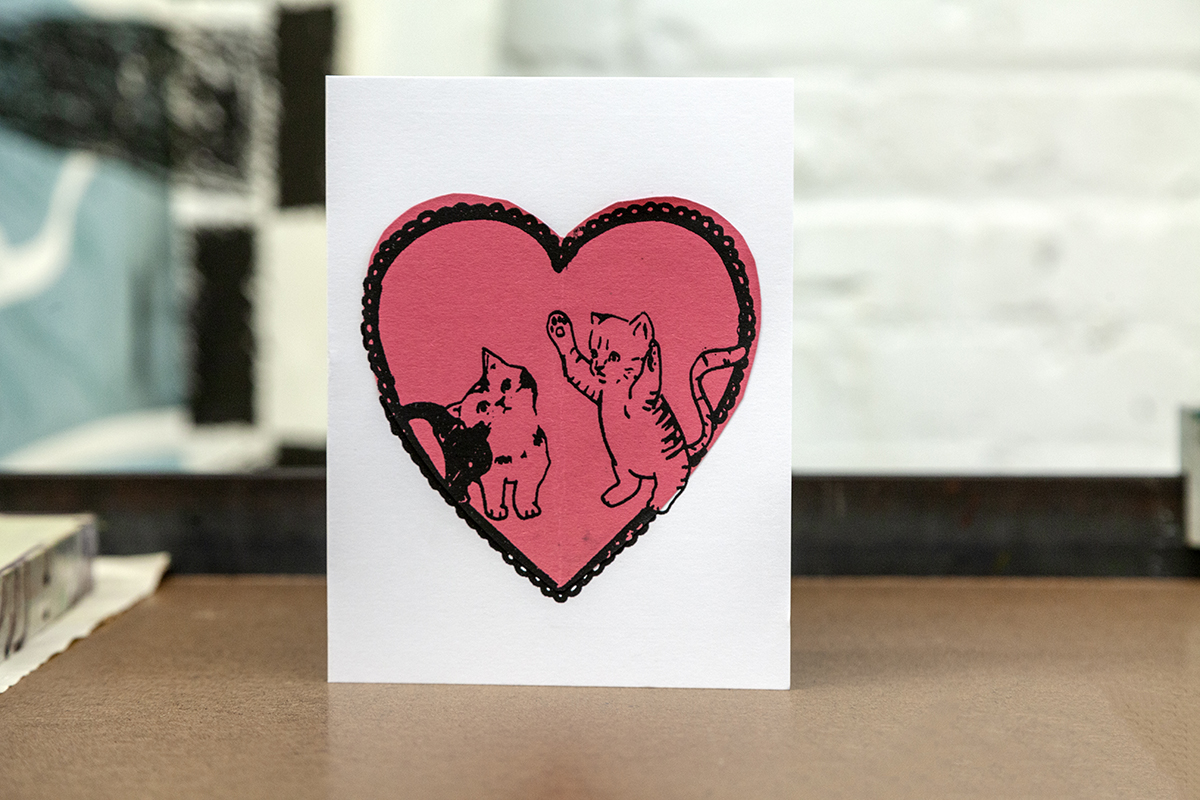 A photo of a Valentine's Day card featuring two playful illustrated cats within an outline of a heart.