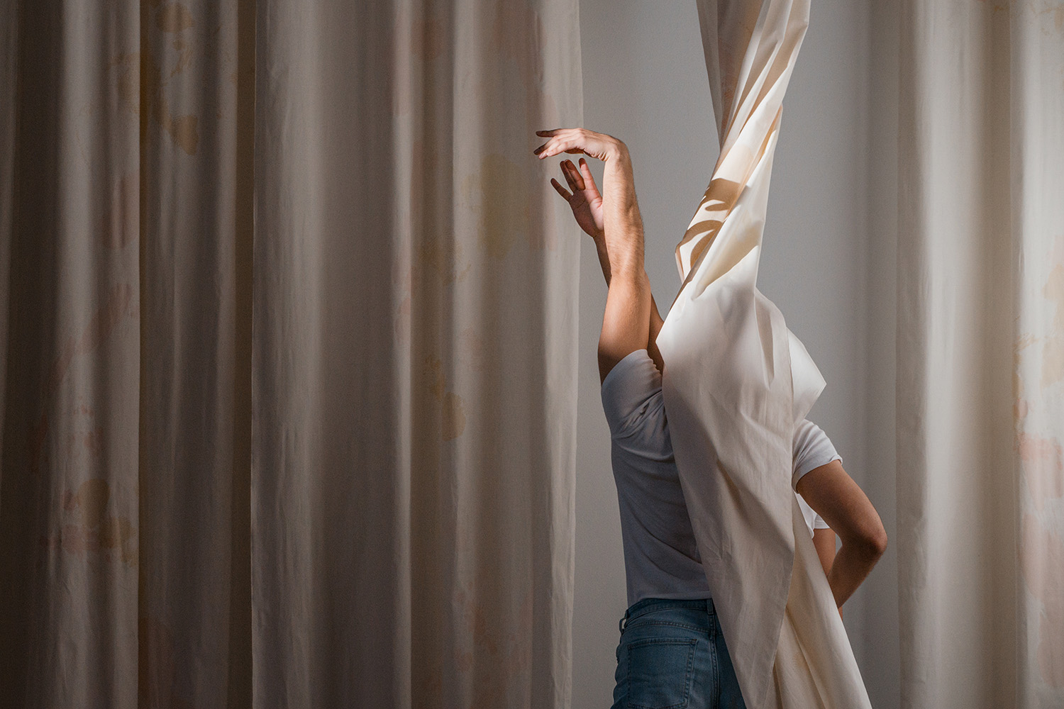 A photo of a performance with dancers hidden behind a curtain, their hands raised upwards to reach one another.