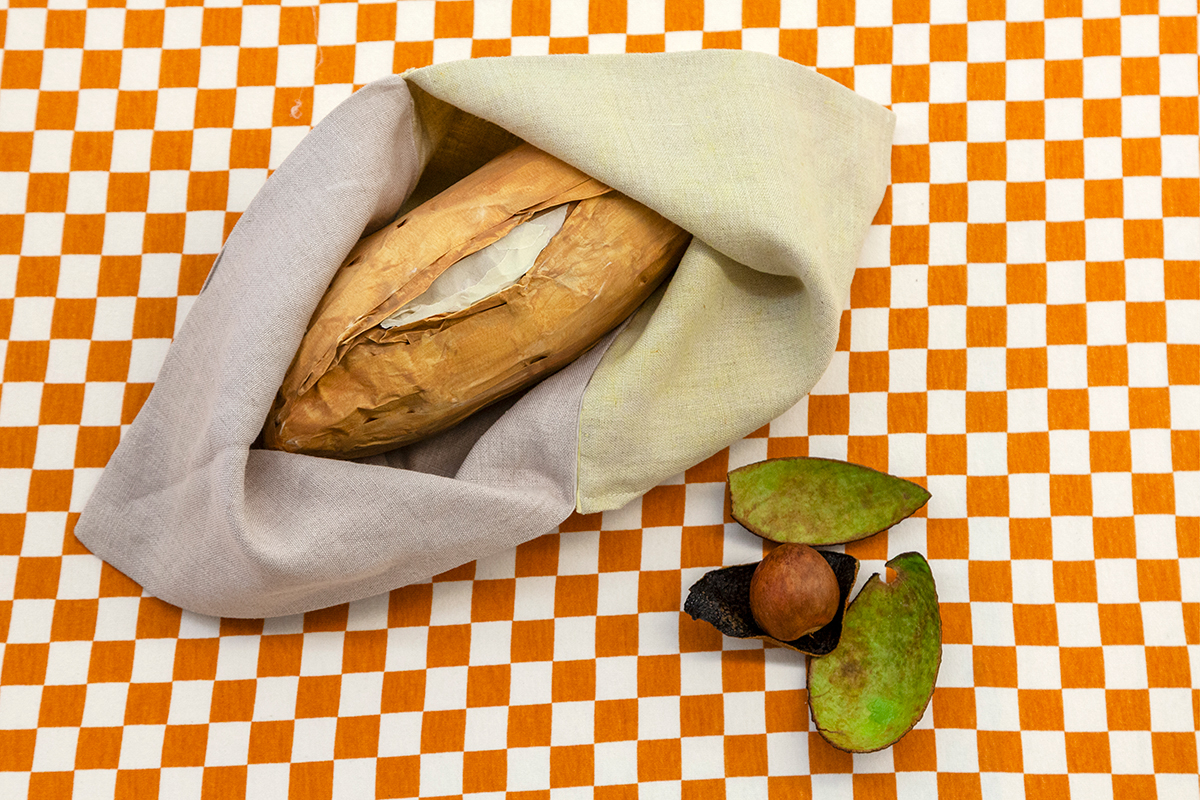 A loaf of bread is nestled in a linen cloth. Nearby, an avocado pit sits on avocado skins that have been scraped clean.