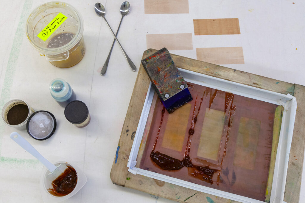 An assortment of natural pigments spread out on a printing table along with a screenprinting frame that has been used for test prints.