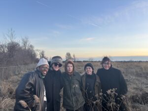Aphotograph of a group of five young adults standing together in a field in the winter smiling for the camera