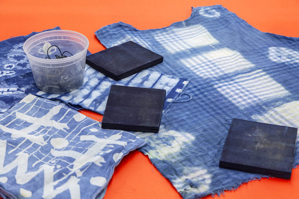 An assortment of fabrics (napkins, bandanas, shirt) that have been dyed in indigo using a shibori technique showing off different dye patterns.