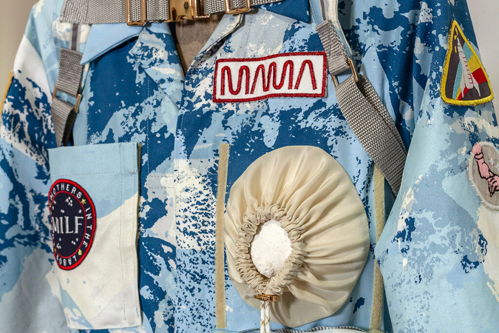 A detail view of a screenprinted space-suit-like garment adorned with patches and pockets.
