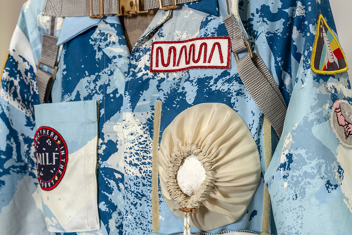 A detail view of a screenprinted space-suit-like garment adorned with patches and pockets.