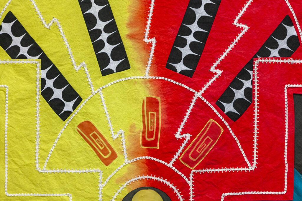 A cropped image of an abstract tapestry dyed yellow and red with lines drawn in white lace. Abstract diamond and rectilinear spiral patterns radiate outward from a half moon shape at the bottom of the composition.