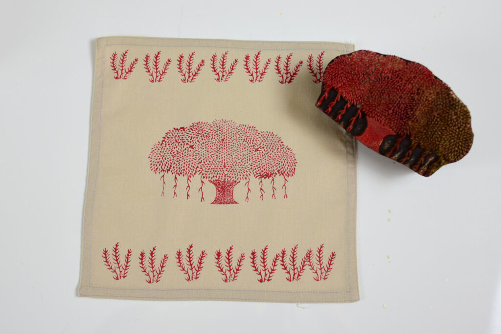 A photograph of a hand-carved woodblock featuring a tree motif laying on top of a printed napkin with the same design as the woodblock.