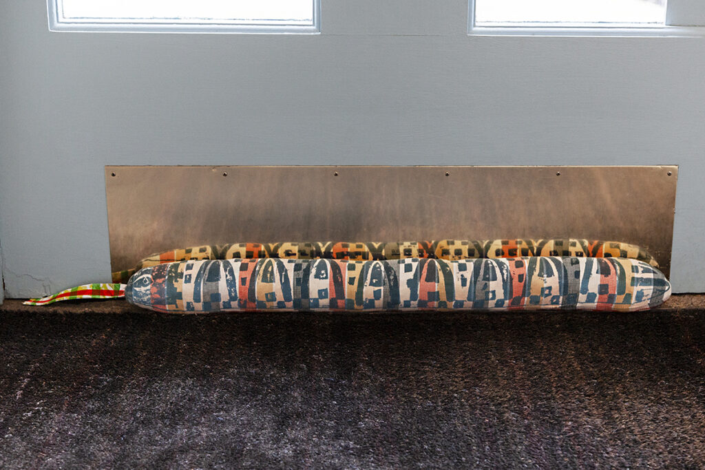 A colorful hand stitched door draft block in the shape of a snake laying against a blue door.