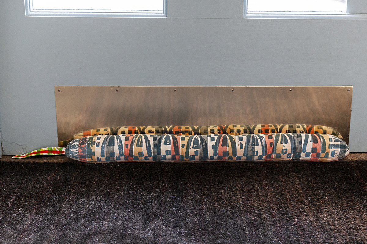 A colorful hand stitched door draft block in the shape of a snake laying against a blue door.