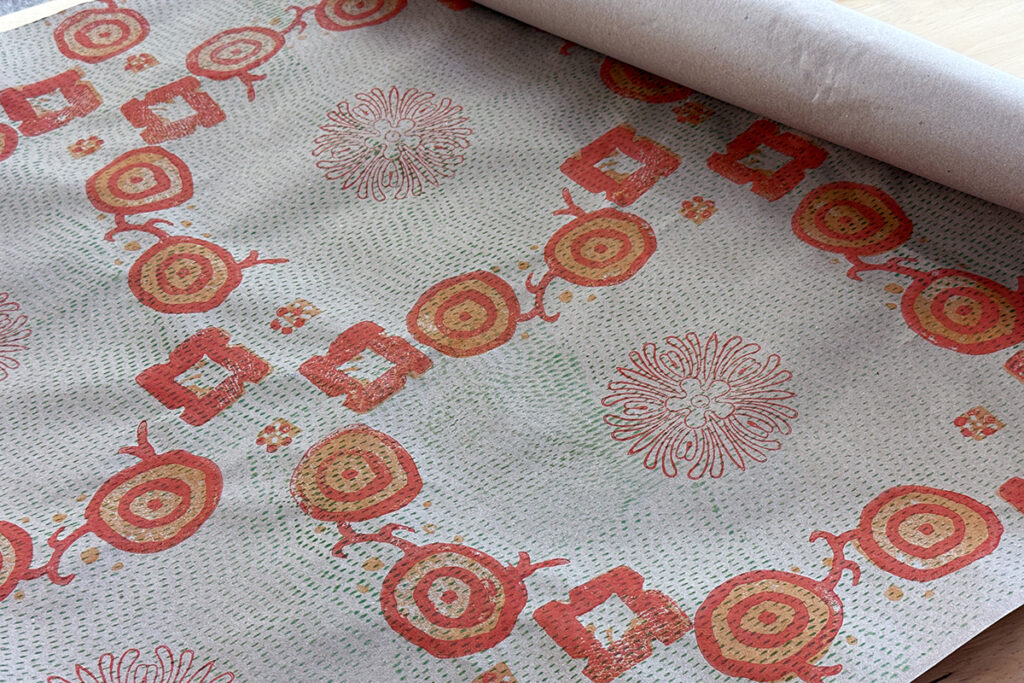 Orange, red, and green block printed shapes create a bold pattern on a roll of craft paper.