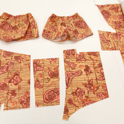 Two pairs of floral boxers laying flat on a table around pieces of cut fabric with the same floral print suggesting they are pattern pieces to make a pair of boxers.