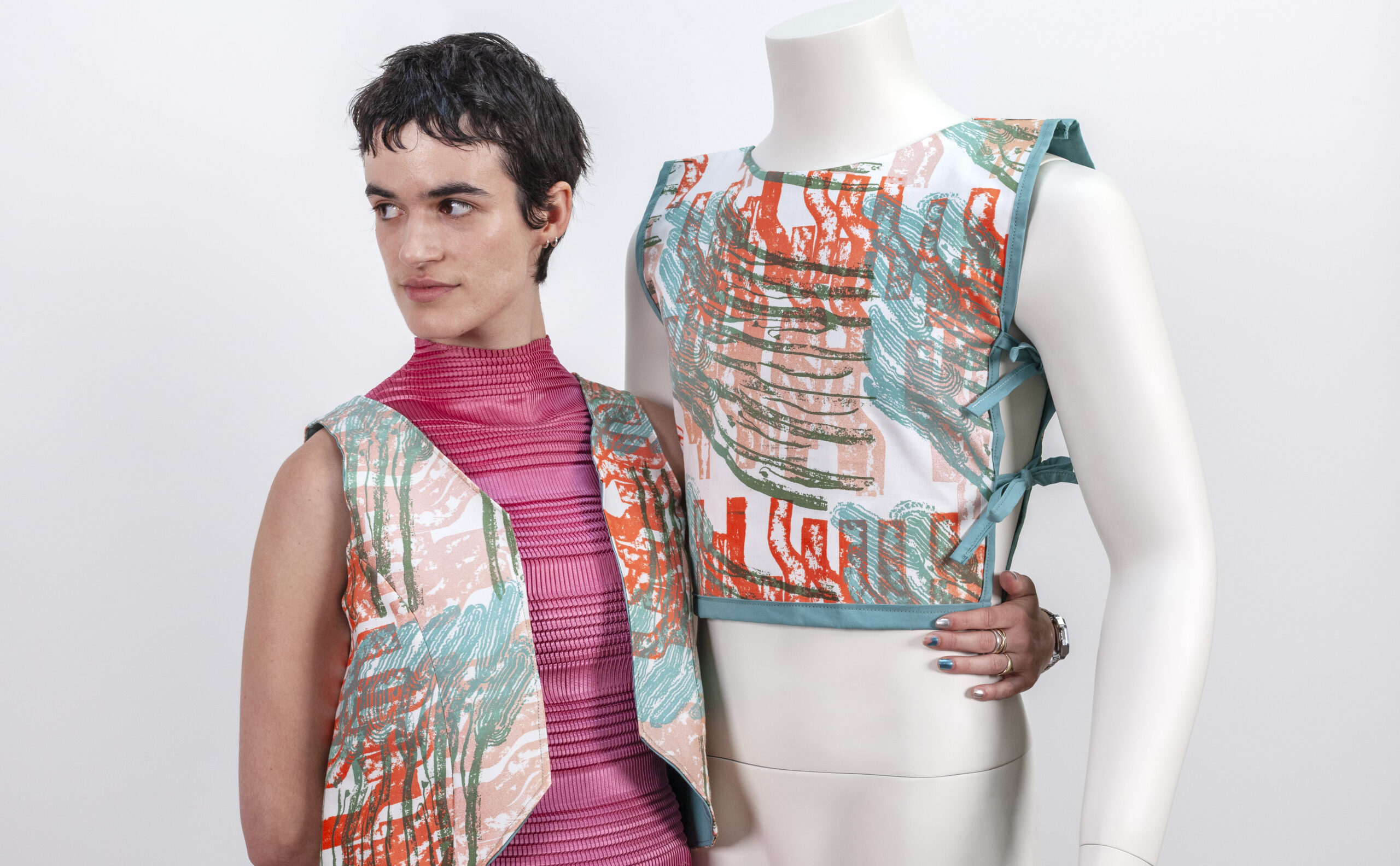 A person and mannequin wearing matching hand-sewn and screenprinted patterned vests in teal, orange, and peach.