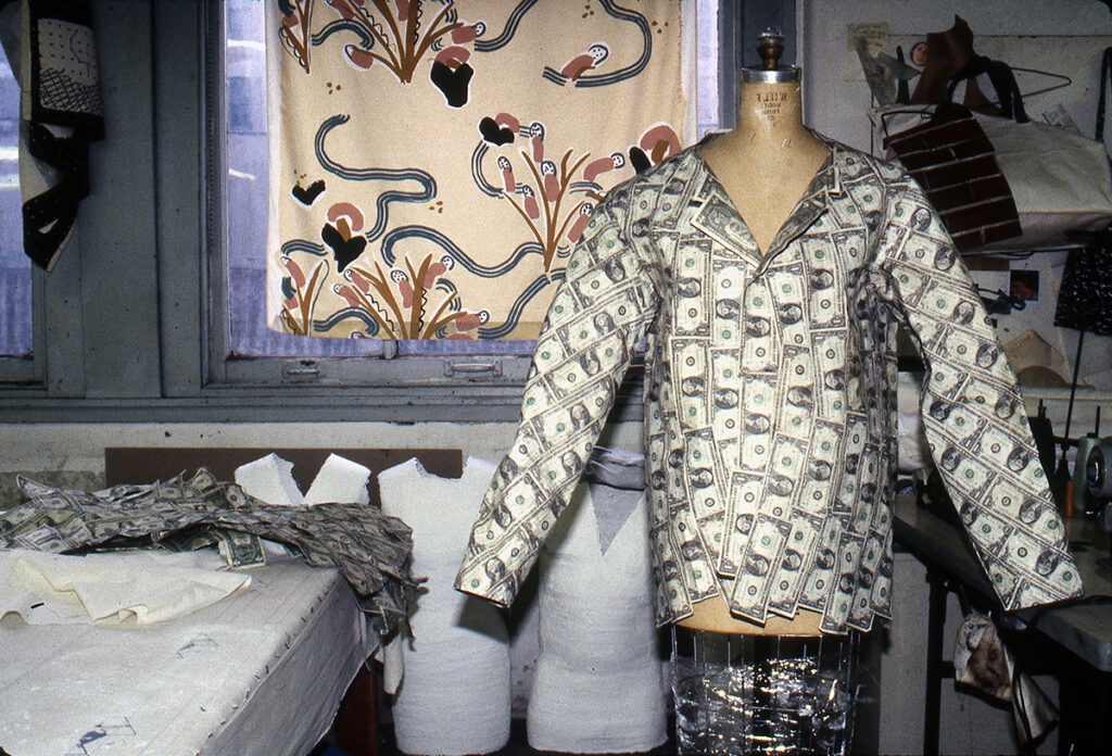 A photo shows a man's suit jacket constructed entirely of US one-dollar bills standing upright on an armature in a studio setting.