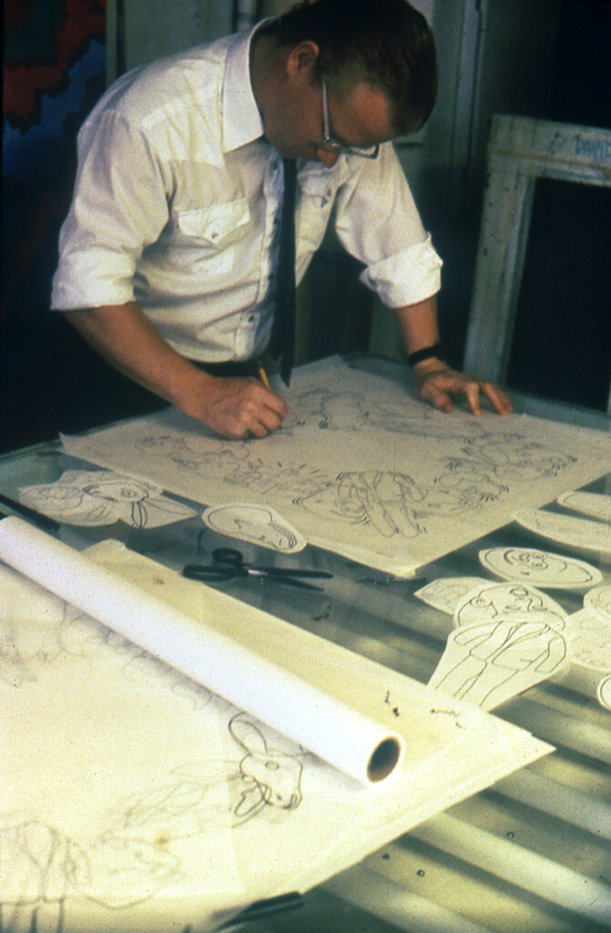 A young artist draws on various pieces of paper over a light table in a studio.