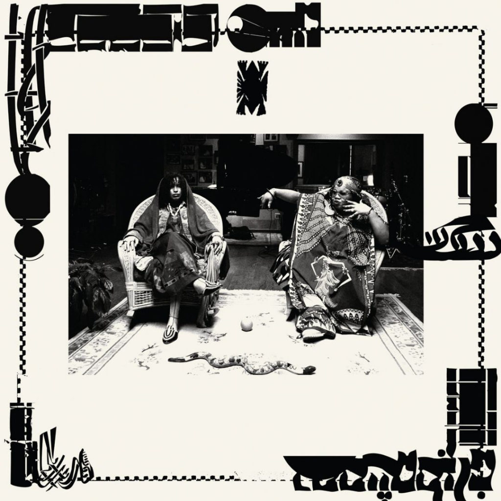 An album cover featuring a photograph of two musicians seated comfortably on large chairs wearing decorative robes. Surrounding the perimeter of the album art are graphic characters of a Middle Eastern language interrupted by blocky and circular shapes.
