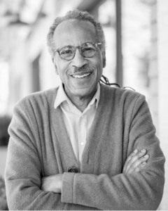 Portrait of Louis Massiah, a Black man wearing glasses and a cardigan.