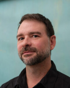 A portrait of Mark Christman, a middle aged white man with short dark hair and a beard.