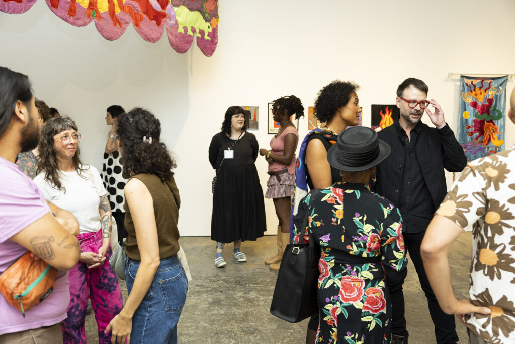 A group of visitors explore a gallery with glimpses of colorful tapestries in the corners of the photo