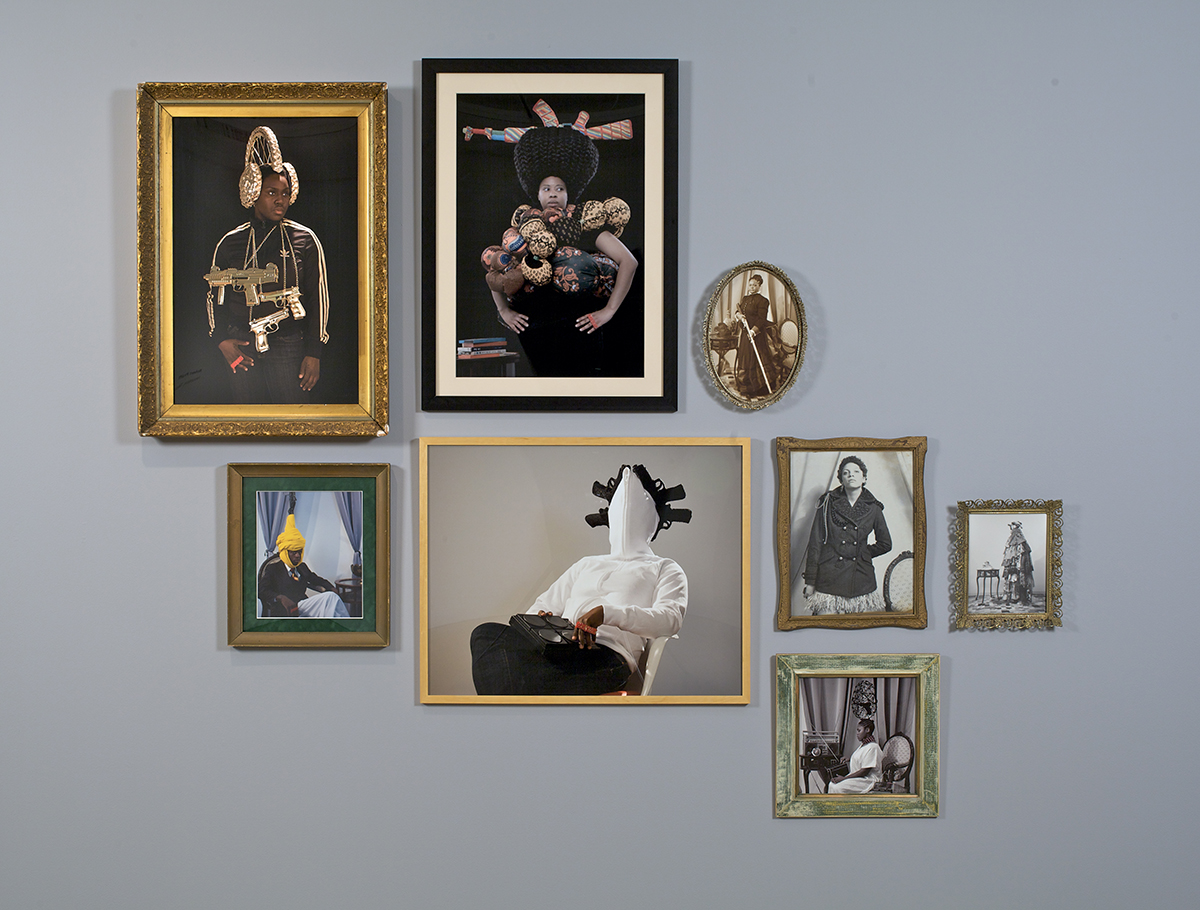 A salon style wall installation of photographs of varying sizes and orientations. The photos are portraits of Black individuals posing with various jewelry, costume, and props.
